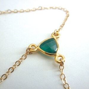 May include: A gold chain necklace with a green gemstone pendant in the shape of a triangle.