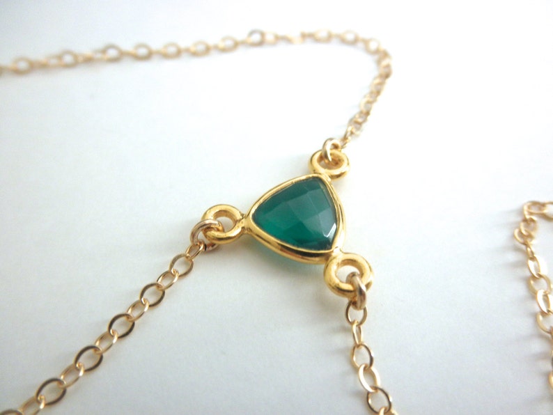 May include: A gold chain necklace with a green gemstone pendant in the shape of a triangle.