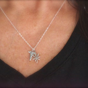 Può includere: Una collana d'argento con un ciondolo che presenta una foglia di marijuana stilizzata e un simbolo di caduceo.