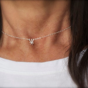 May include: A silver chain necklace with a small marijuana leaf pendant. The necklace is worn by a person with long dark hair.