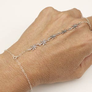 May include: A silver chain bracelet with a delicate design featuring multiple small star-shaped charms. The bracelet is adjustable and can be worn on the wrist or as a finger ring.