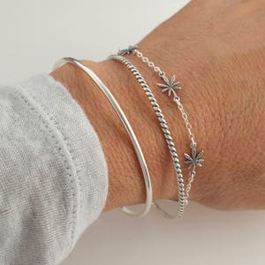 Pu&ograve; includere: Tre braccialetti d'argento impilati su un polso. Il braccialetto superiore &egrave; una catena delicata con piccoli ciondoli a forma di foglia d'argento. Il braccialetto centrale &egrave; una fascia d'argento intrecciata. Il braccialetto inferiore &egrave; una fascia sottile e liscia d'argento.