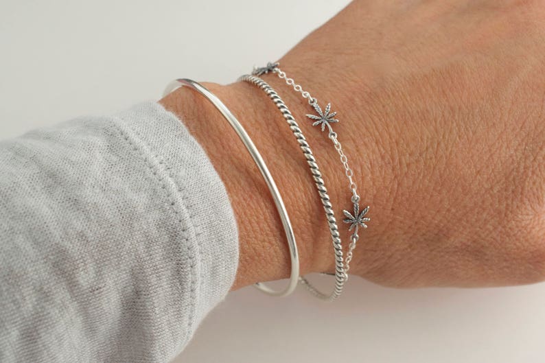 Pu&ograve; includere: Tre braccialetti d'argento impilati su un polso. Il braccialetto superiore &egrave; una catena delicata con piccoli ciondoli a forma di foglia d'argento. Il braccialetto centrale &egrave; una fascia d'argento intrecciata. Il braccialetto inferiore &egrave; una fascia sottile e liscia d'argento.