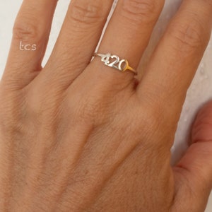 May include: A silver ring with the number "420" on it. The ring is worn on a person's finger.