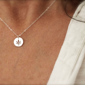 Può includere: Una collana d'argento con un ciondolo rotondo con un design a foglia di marijuana tagliata.