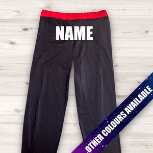 May include: Black leggings with a red waistband and the word "NAME" printed in white on the front. The leggings are photographed against a woodgrain background. A banner at the bottom of the image reads "OTHER COLORS AVAILABLE".