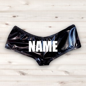 May include: Black shiny shorts with the word "NAME" printed in white on the front.
