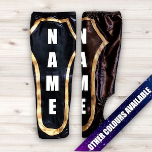 May include: Two pairs of black and brown wrestling tights with gold trim. The tights have the word "NAME" written vertically on the front. Other colors are available.
