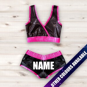 May include: Black and pink wrestling outfit with a black top and shorts. The shorts have the word "NAME" printed on the back.