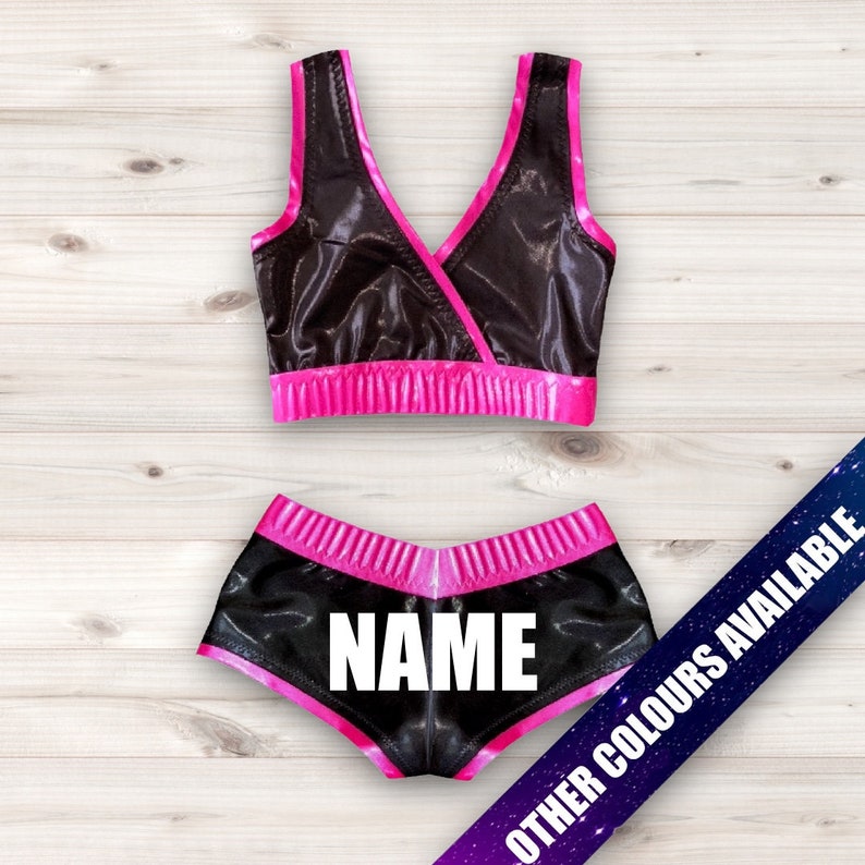 May include: Black and pink wrestling outfit with a black top and shorts. The shorts have the word "NAME" printed on the back.