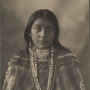 May include: Black and white portrait photograph of a Native American woman wearing a beaded necklace and traditional clothing. The text "Hattietom Apache" is written below the image.