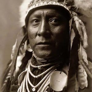 May include: A black and white portrait of a Native American man wearing a traditional headdress with feathers and a beaded necklace.