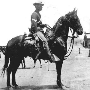 Puede incluir: Una fotograf&iacute;a en blanco y negro de un hombre con uniforme montando a caballo. El hombre lleva un sombrero y sostiene las riendas. El caballo lleva una brida y tiene una silla de montar.
