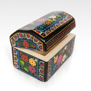 May include: A small, open wooden chest with a black exterior, adorned with colorful floral patterns. The lid is slightly ajar, revealing the natural wood interior. The chest features a rectangular base and a curved, arched lid.