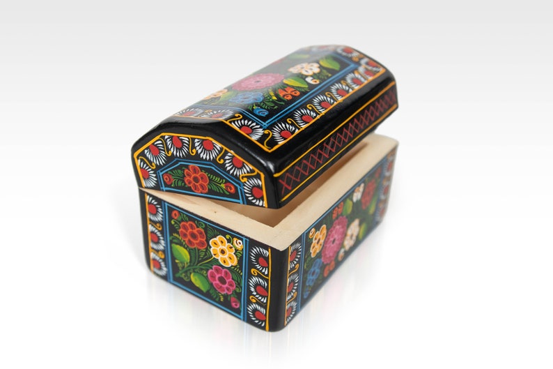 May include: A small, open wooden chest with a black exterior, adorned with colorful floral patterns. The lid is slightly ajar, revealing the natural wood interior. The chest features a rectangular base and a curved, arched lid.