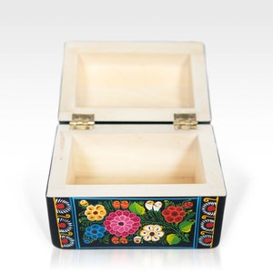 May include: Open wooden box with a black exterior and floral design. The box is rectangular with a hinged lid and brass-colored hinges. The floral design includes pink, red, yellow, and blue flowers with green leaves. The interior of the box is light-colored wood.