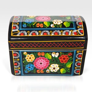 May include: Black wooden chest with a curved top, hand-painted with colorful floral designs. The chest features pink, blue, yellow, and white flowers with green leaves. The edges are decorated with red and yellow geometric patterns.