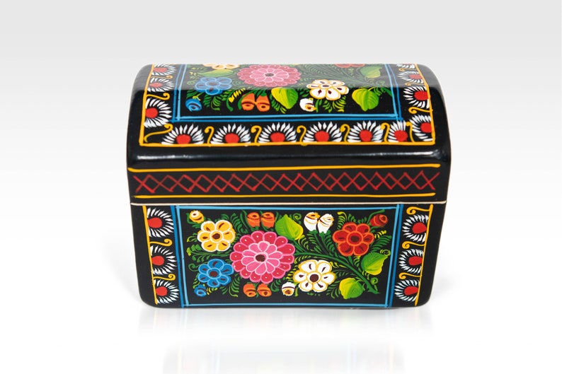 May include: Black wooden chest with a curved top, hand-painted with colorful floral designs. The chest features pink, blue, yellow, and white flowers with green leaves. The edges are decorated with red and yellow geometric patterns.