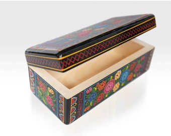 May include: A black wooden box with a floral design painted on the sides and lid. The lid is open, revealing the empty interior.