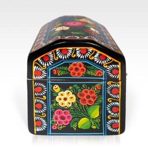 May include: A black, arched-top wooden box with vibrant floral designs. The box features red, yellow, and pink flowers with green leaves against a black background. The edges are decorated with white and blue patterns.