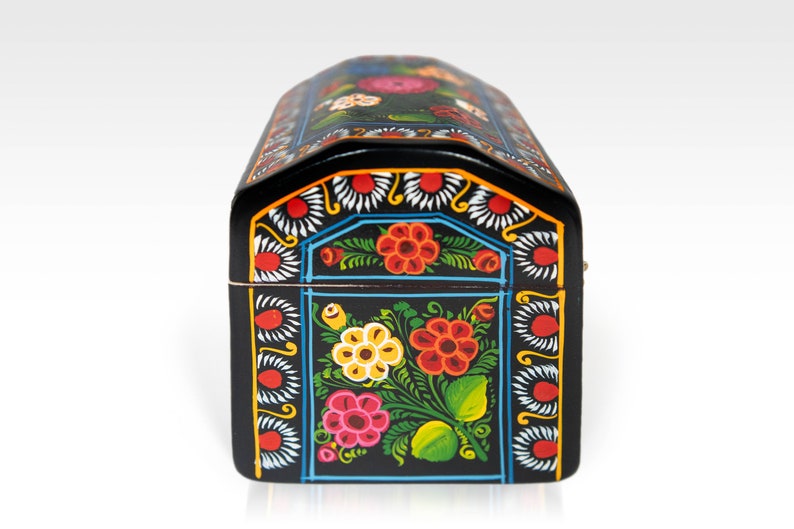 May include: A black, arched-top wooden box with vibrant floral designs. The box features red, yellow, and pink flowers with green leaves against a black background. The edges are decorated with white and blue patterns.