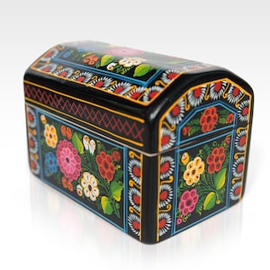 May include: A black wooden chest with a curved top, adorned with vibrant floral patterns in pink, red, yellow, and blue. The chest features intricate detailing and a glossy finish, perfect for storing small items.