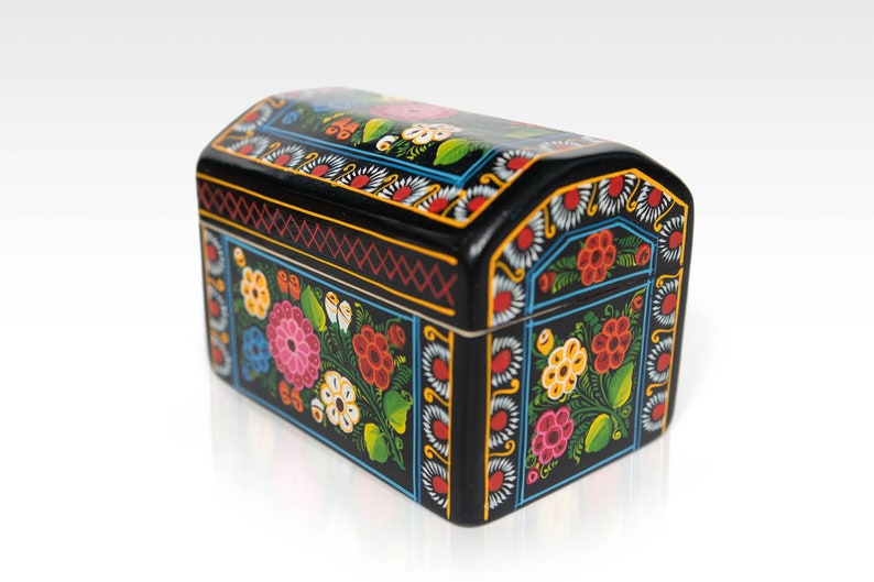 May include: A black wooden chest with a curved top, adorned with vibrant floral patterns in pink, red, yellow, and blue. The chest features intricate detailing and a glossy finish, perfect for storing small items.