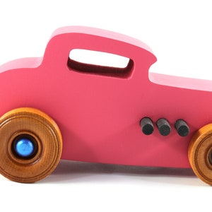 This is a handmade wooden Hot Rod '32 Deuce Coupe toy car. It is hand-painted hot pink with black and metallic sapphire blue trim. The hardwood wheels are finished with nonmarring amber shellac.