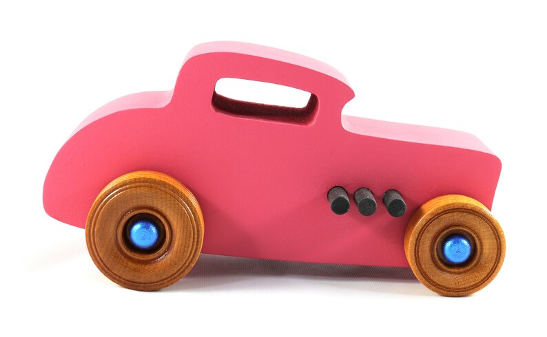 This is a handmade wooden Hot Rod '32 Deuce Coupe toy car. It is hand-painted hot pink with black and metallic sapphire blue trim. The hardwood wheels are finished with nonmarring amber shellac.