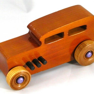 This is a handmade wooden toy car modeled after a Hot Rod 1932 Ford Sedan. It is made from wood, finished with multiple coats of amber shellac, and trimmed with black and metallic purple acrylic paint.