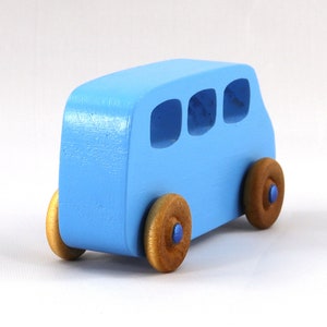 May include: A light blue wooden toy bus with three windows and four brown wheels. The bus is painted a light blue color and has a simple design.