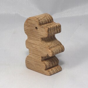 May include: A wooden toy shaped like a standing dinosaur. The toy is made of light brown wood and has a smooth, polished finish.
