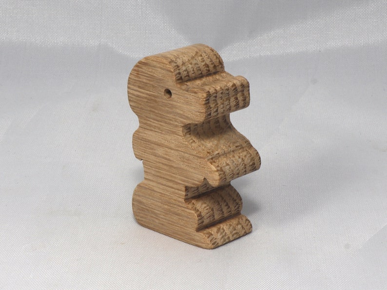 May include: A wooden toy shaped like a standing dinosaur. The toy is made of light brown wood and has a smooth, polished finish.