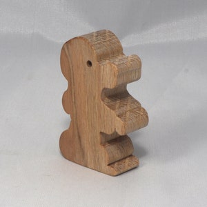 May include: A wooden toy shaped like a standing dinosaur. The toy is made of light brown wood and has a simple, cartoon-like design.