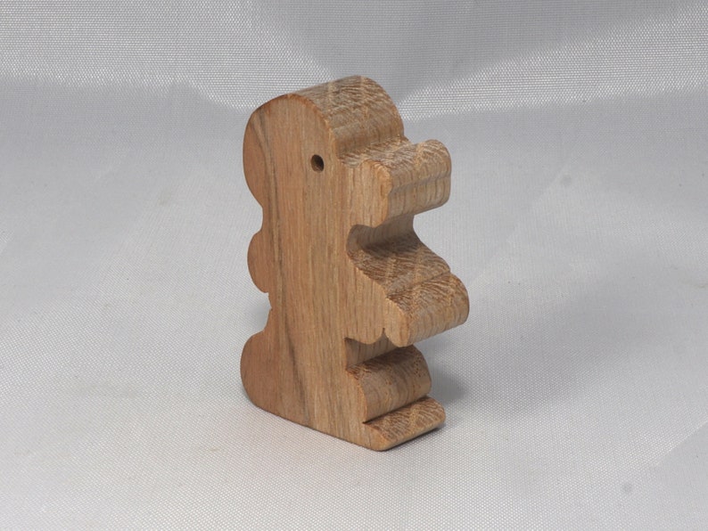 May include: A wooden toy shaped like a standing dinosaur. The toy is made of light brown wood and has a simple, cartoon-like design.