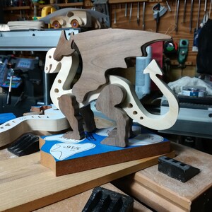 Handmade wooden dragon figurine made from contrasting hardwoods with a light natural wood body and head paired with rich dark reddish-brown wings, legs, and horns. Displayed in my shop prior to finishing.