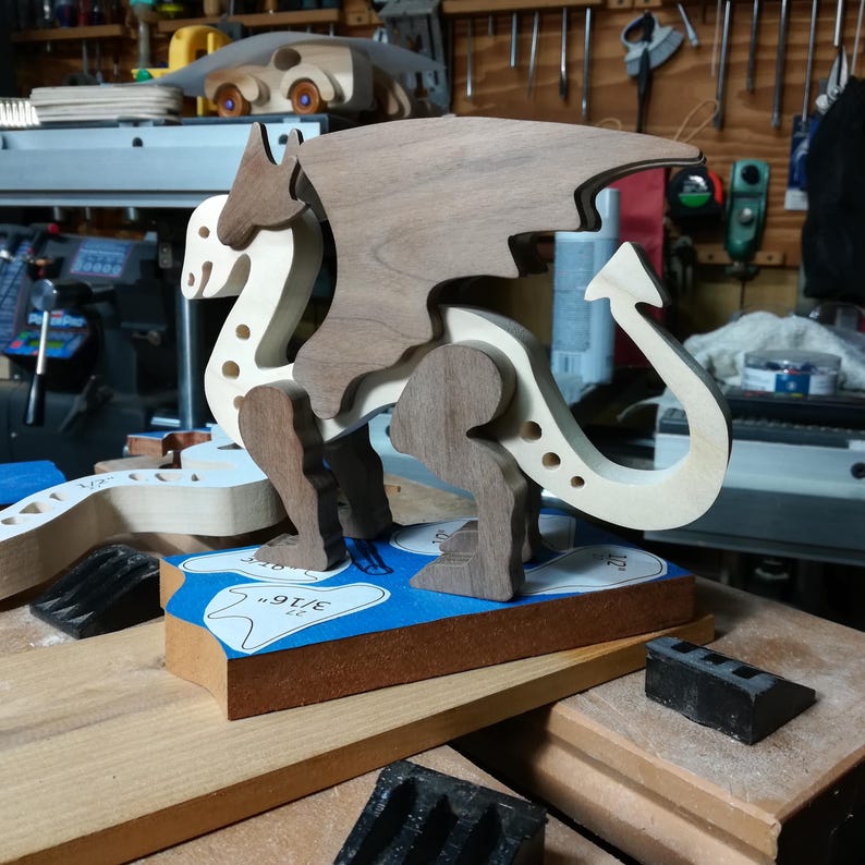 Handmade wooden dragon figurine made from contrasting hardwoods with a light natural wood body and head paired with rich dark reddish-brown wings, legs, and horns. Displayed in my shop prior to finishing.