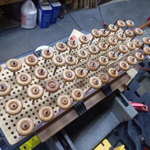 Rows of amber-finished wooden toy truck wheels mounted on dowels in a perforated board in the workshop.