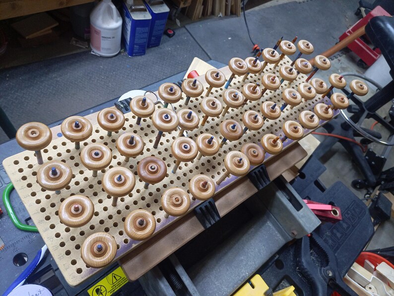 Rows of amber-finished wooden toy truck wheels mounted on dowels in a perforated board in the workshop.