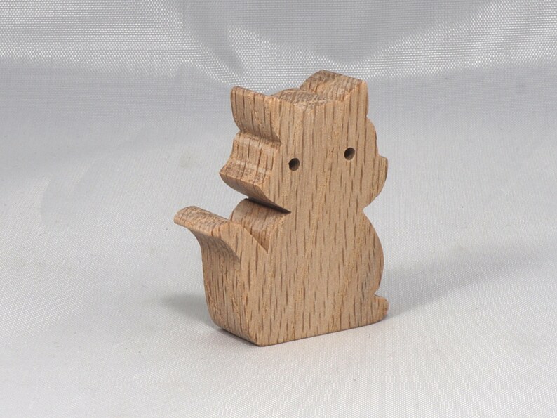 May include: A wooden squirrel figurine with a light brown finish. The squirrel is standing on its hind legs with its tail curled behind it.