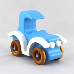 May include: A blue wooden toy car with white accents and brown wheels. The car has a rounded, curved roof and headlights.