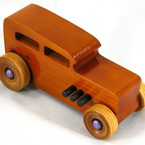 This is a handmade wooden toy car modeled after a Hot Rod 1932 Ford Sedan. It is made from wood, finished with multiple coats of amber shellac, and trimmed with black and metallic purple acrylic paint.