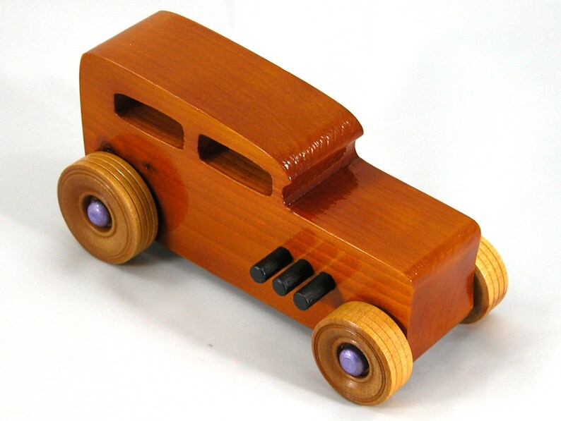 This is a handmade wooden toy car modeled after a Hot Rod 1932 Ford Sedan. It is made from wood, finished with multiple coats of amber shellac, and trimmed with black and metallic purple acrylic paint.