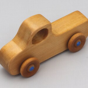 Wooden toy pickup truck from the Play Pal Collection at Odin's Toy Factory. Made from natural wood, finished with amber shellac, and accented with metallic sapphire blue acrylic paint on the wheel hubs. Made In The USA. Approximate dimensions: length 3-1/2 inches, height 1-3/8 inches, width 1-1/2 inches, wheels 3/4 inch diameter. Handmade in Tallahassee, Florida. Natural wood grain and color variations.