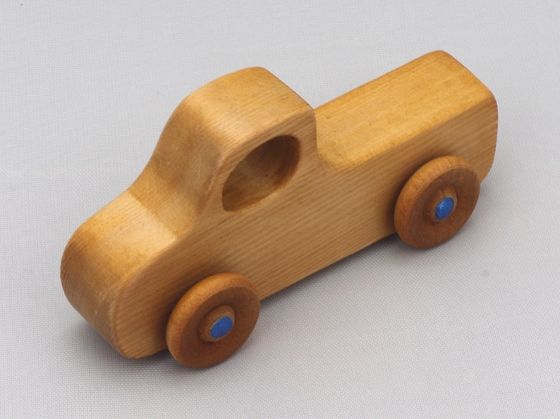 Wooden toy pickup truck from the Play Pal Collection at Odin's Toy Factory. Made from natural wood, finished with amber shellac, and accented with metallic sapphire blue acrylic paint on the wheel hubs. Made In The USA. Approximate dimensions: length 3-1/2 inches, height 1-3/8 inches, width 1-1/2 inches, wheels 3/4 inch diameter. Handmade in Tallahassee, Florida. Natural wood grain and color variations.