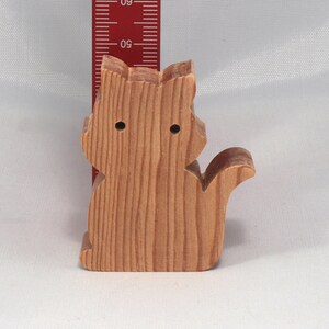 May include: A wooden cat figurine, carved from light brown wood. The cat is sitting with its tail curled around its body. The figurine is about 4 inches tall.