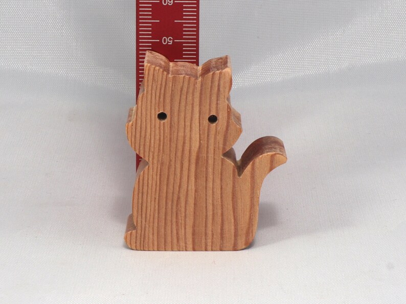 May include: A wooden cat figurine, carved from light brown wood. The cat is sitting with its tail curled around its body. The figurine is about 4 inches tall.