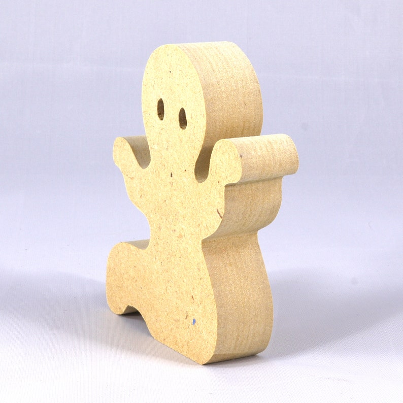 A handmade, unpainted wooden ghost cutout stands upright on a white background. The light-colored solid wood figure has a rounded head with two circular eye cutouts, raised wavy arms, and a curved wavy base, ready for painting or crafting.