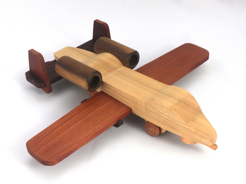 May include: A wooden toy airplane with a natural wood finish, featuring dark brown engine housings and wings, and reddish-brown wings and tail. The toy has small wooden wheels and is designed for play.