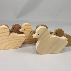 Five wooden duck figurines in various shades of brown and beige. The ducks are all facing the same direction and are arranged in a row.